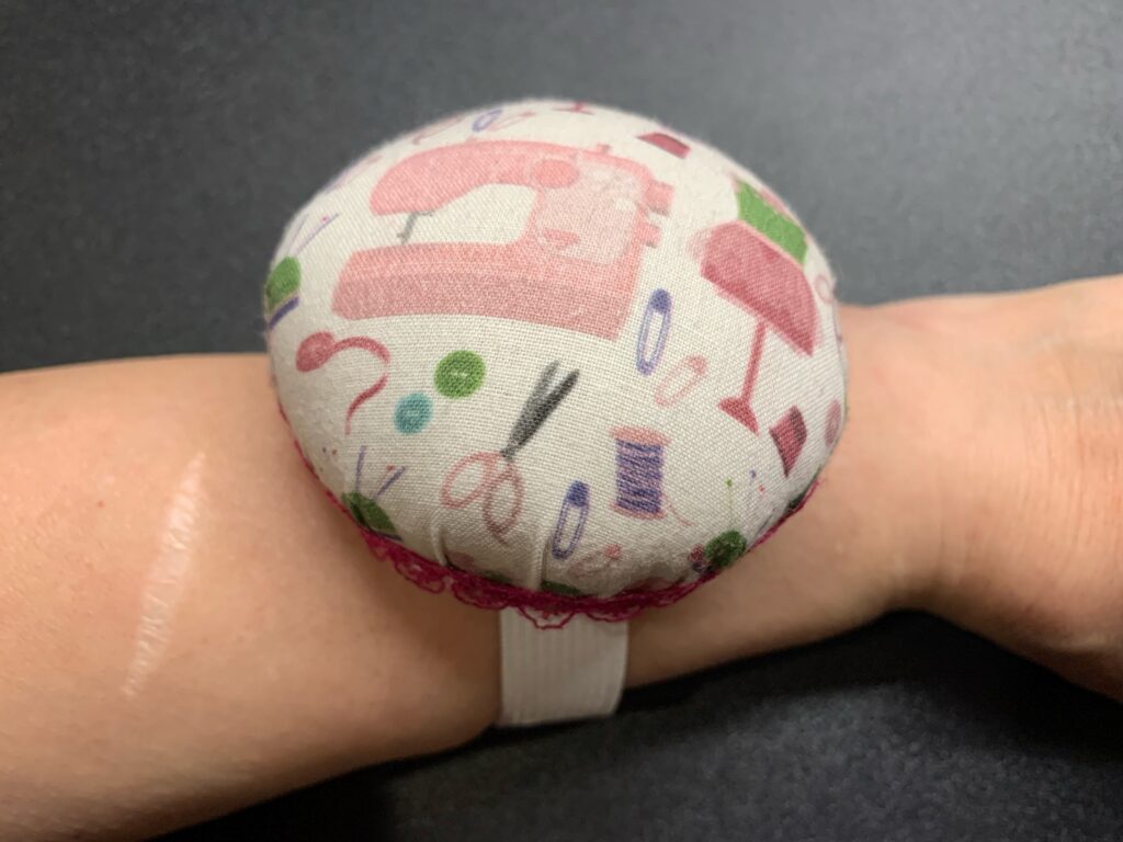 Acerico de tela con dibujos de costura colocado en la muñeca