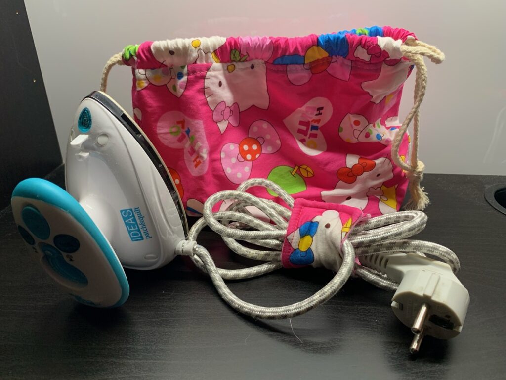 Plancha pequeña junto a su bolsa de tela rosa de Hello Kitty y el cable recogido con un sujetacables a juego