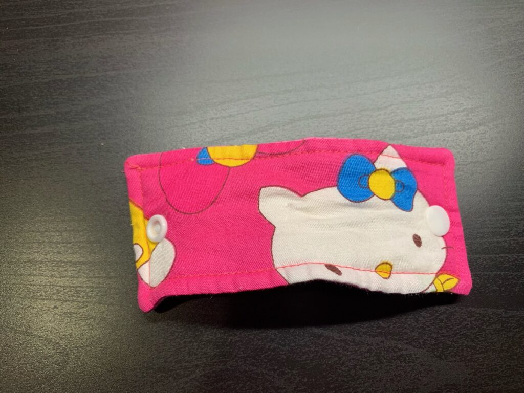Cable de una plancha pequeña recogido con un sujetacables de tela rosa de Hello Kitty y broches a presión de colores