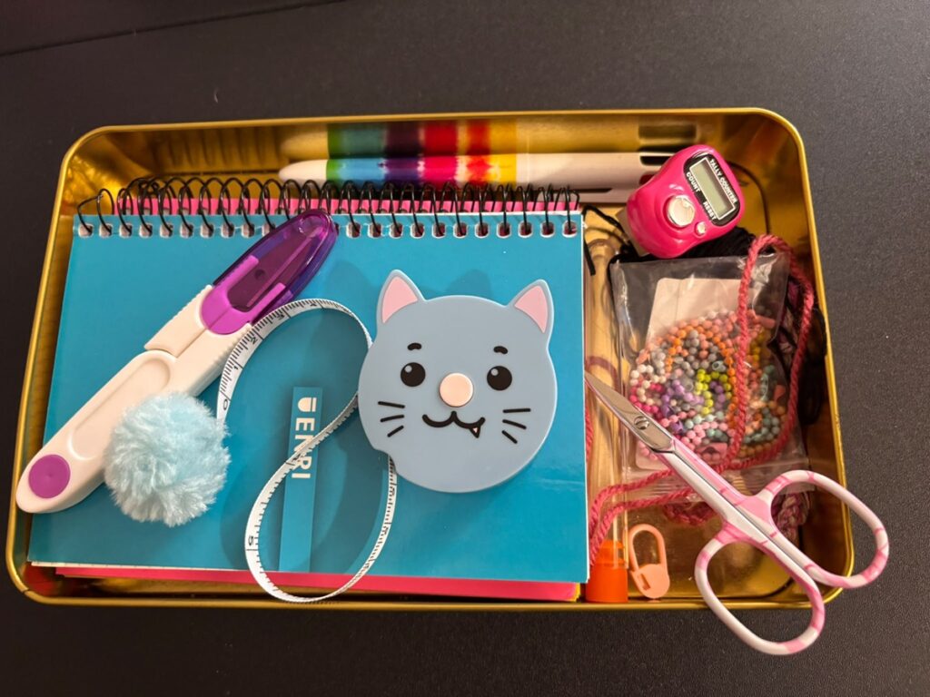 Bandeja con accesorios de crochet, como marcadores, contador de vueltas, cinta métrica y tijeras.