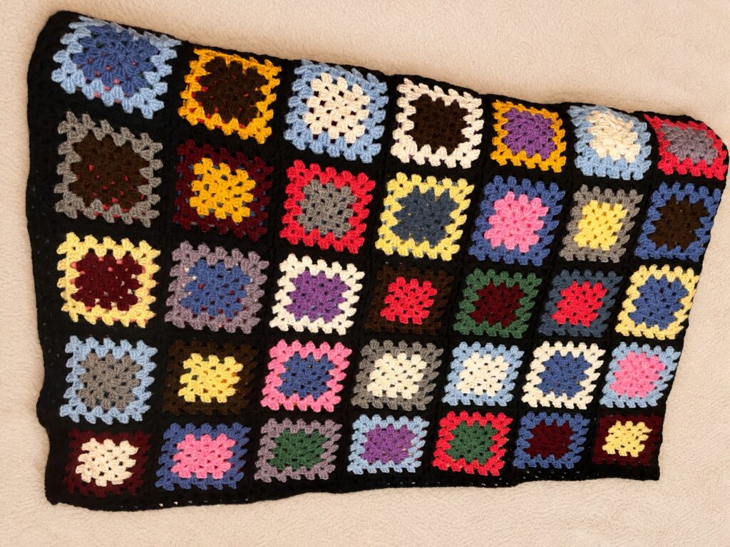 Manta de crochet hecha por Drioky con granny squares de distintos colores y borde negro