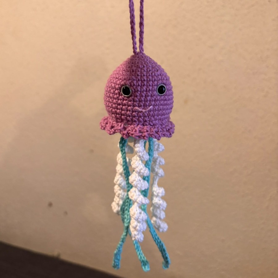 Medusa amigurumi de crochet rosa, con tentáculos blancos y turquesa, colgada en una pared.