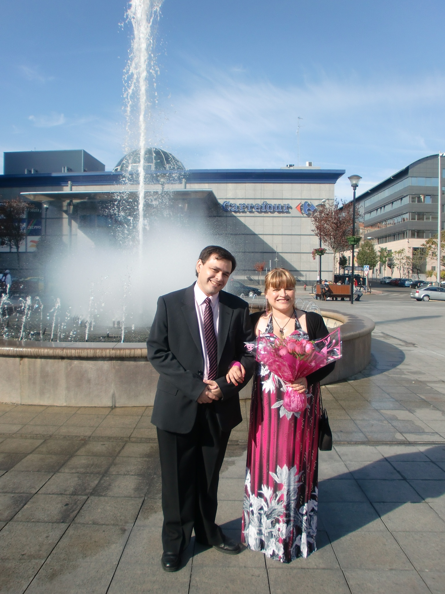 Fotografía original de una pareja después de su boda civil, posando junto a una fuente con un ramo de flores.