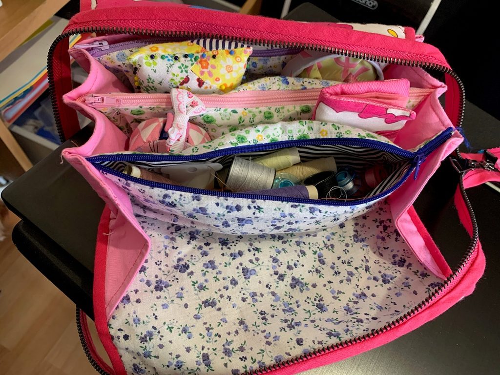 Costurero de viaje abierto con varios compartimentos con cremallera y accesorios de costura en su interior.